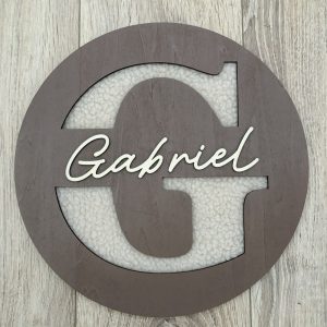 Plaque de porte ronde en bois taupe, initiale G sur fond bouclette et prenom Gabriel en relief